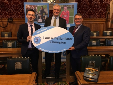 Graham holding an OK Foundation Sign, reading "I am a Defibrillator Champion"